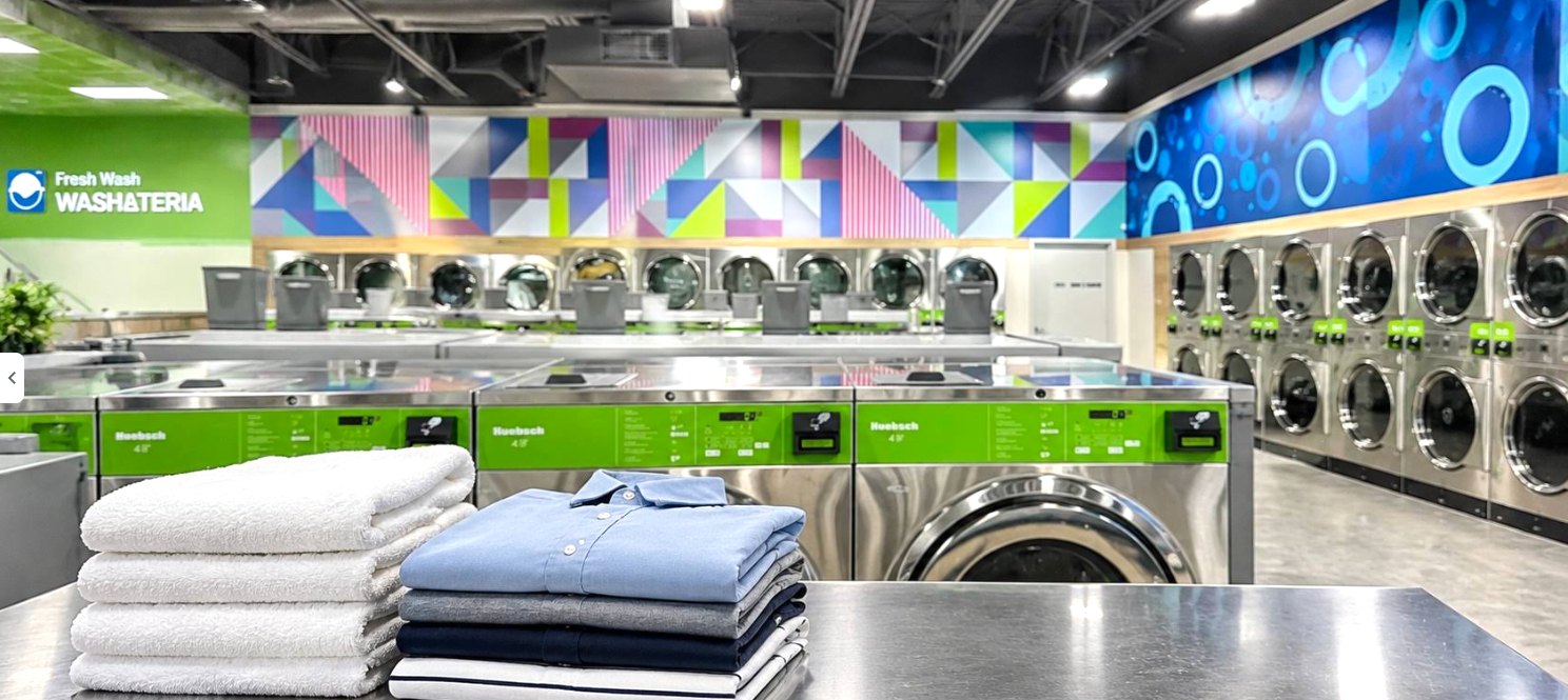 Inside Fresh Wash Washateria: folded towels and shirts on a stainless folding table in front of rows of washers